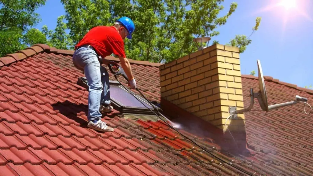 a roofer performing moss removal on a tile roof