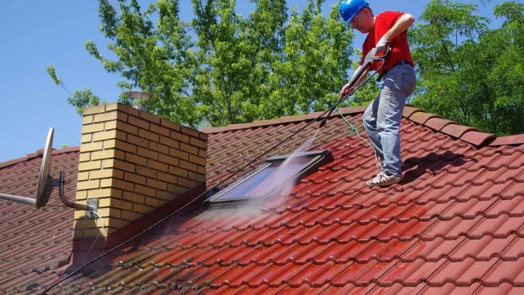 a roofer using a pressure washer to clean a roof