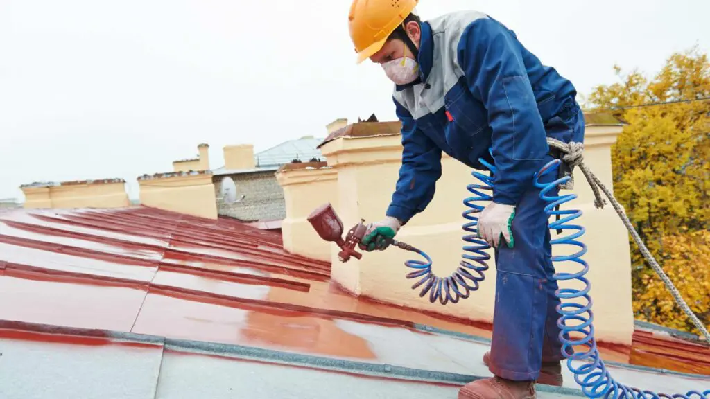 a roofer using a spray gun to paint a metal roof