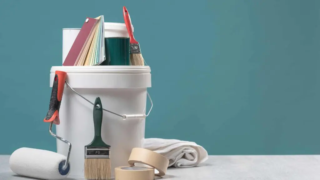 a bucket of roof paint, some paintbrushes a paint roller and other painting materials
