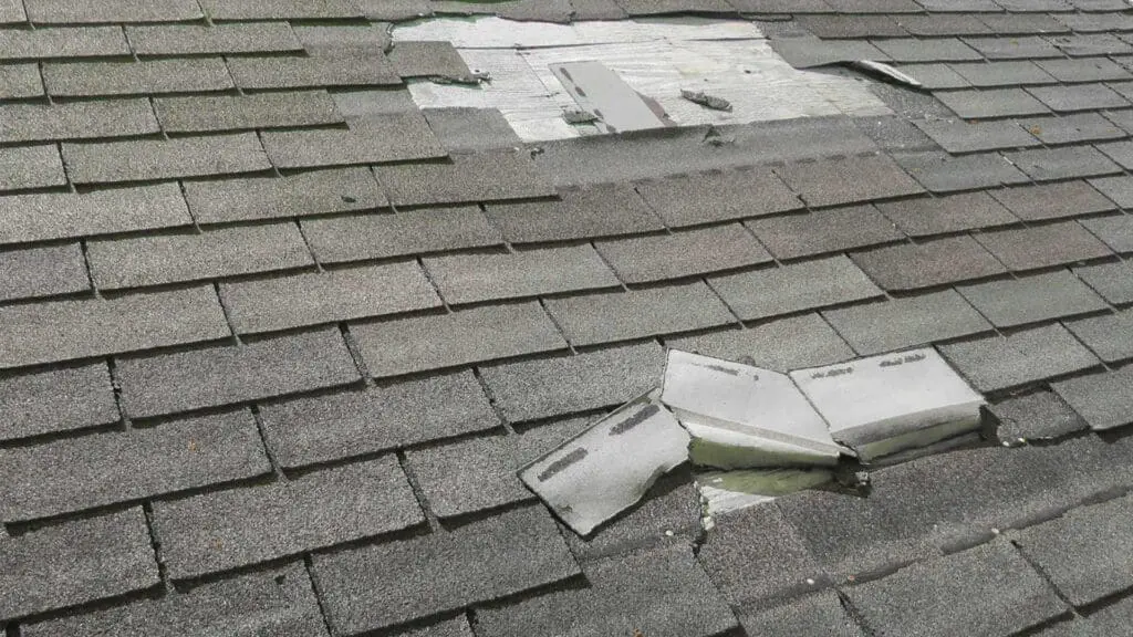 an asphalt shingle roof showing signs of wind damage with multiple shingles blown back due to wind.