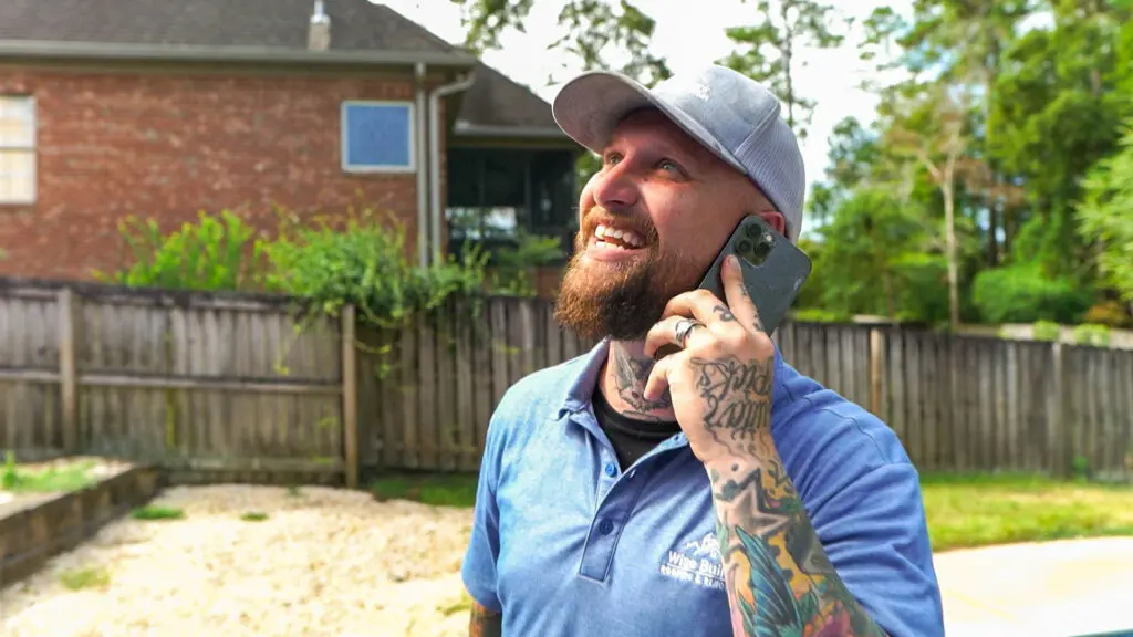 a roofer from wise builders roofing and renovations llc on the phone smiling at a new roof being installed on an alabama house
